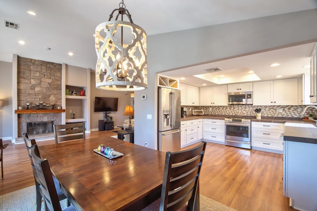 dining space with a stone fireplace, light wood-type flooring, and sink