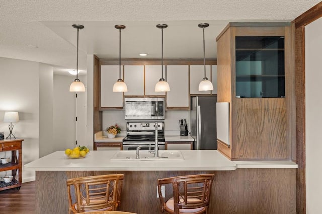 kitchen with a textured ceiling, dark hardwood / wood-style floors, stainless steel appliances, and hanging light fixtures