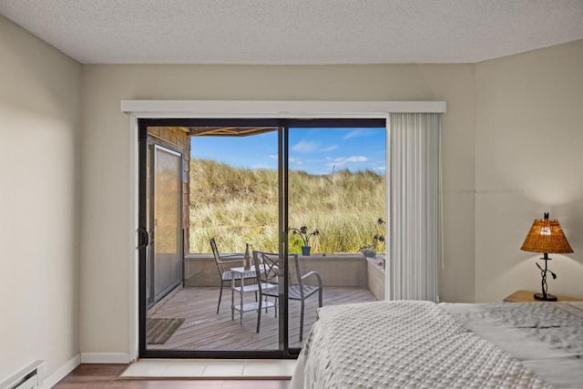 bedroom with light wood-type flooring, a textured ceiling, access to exterior, and a baseboard heating unit