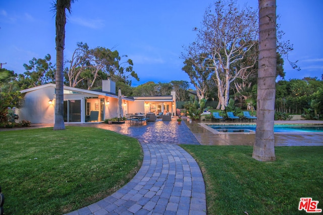 back house at dusk with a lawn and a patio