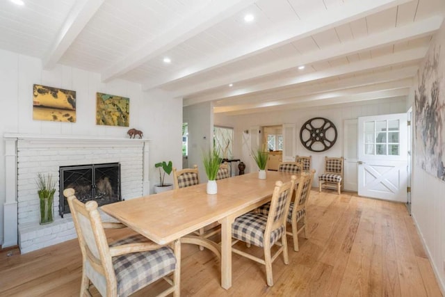 dining space featuring beam ceiling, a fireplace, and light wood-type flooring