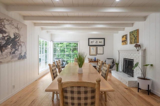 dining area featuring beam ceiling, light wood-type flooring, a fireplace, and wooden walls