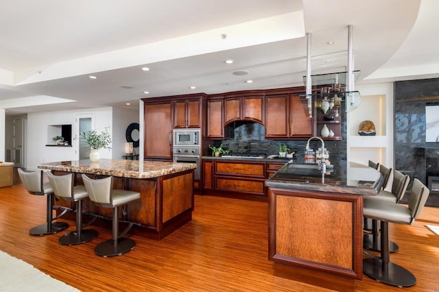 kitchen with premium range hood, appliances with stainless steel finishes, a breakfast bar area, hardwood / wood-style flooring, and tasteful backsplash