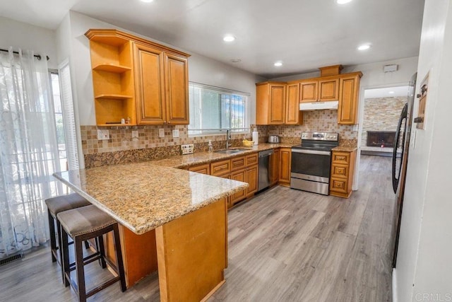 kitchen with a kitchen breakfast bar, light hardwood / wood-style flooring, stainless steel appliances, backsplash, and sink