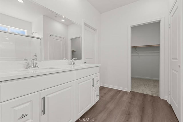 bathroom with double vanity, wood finished floors, a stall shower, and a sink