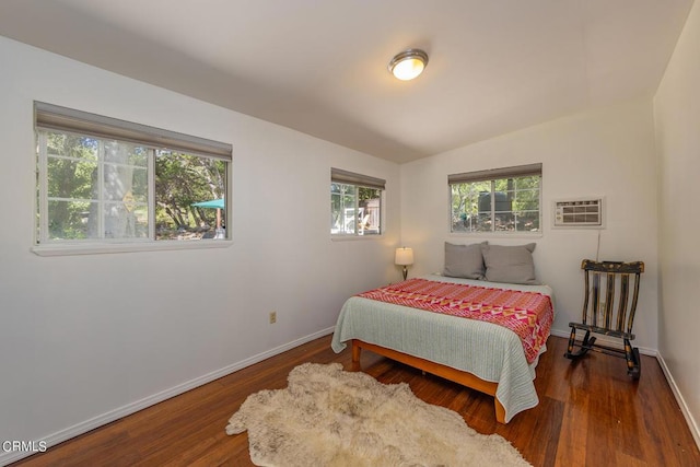 bedroom featuring dark hardwood / wood-style floors, vaulted ceiling, a wall unit AC, and multiple windows