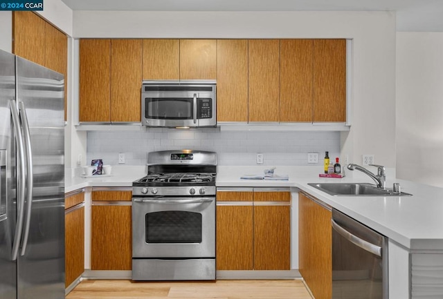 kitchen with backsplash, sink, stainless steel appliances, and light wood-type flooring