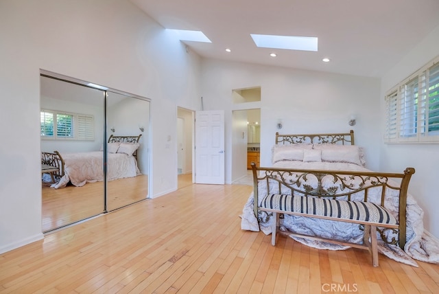 bedroom with light hardwood / wood-style floors, high vaulted ceiling, a skylight, and a closet