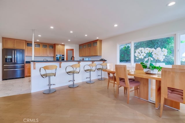 kitchen with light wood-type flooring, kitchen peninsula, stainless steel oven, a breakfast bar area, and fridge with ice dispenser