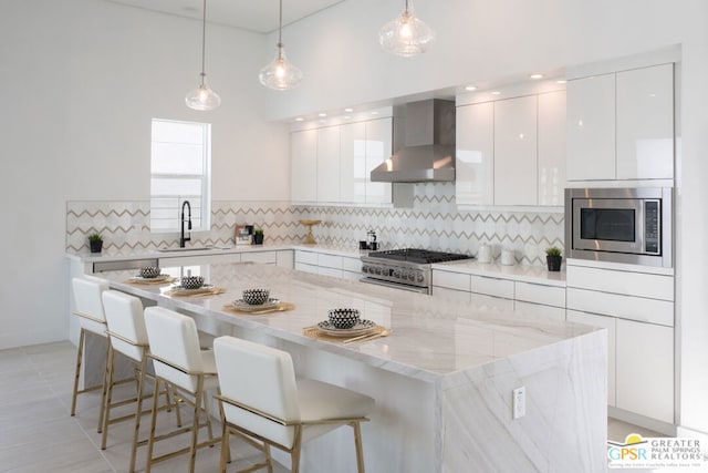 kitchen featuring stainless steel appliances, sink, wall chimney range hood, pendant lighting, and white cabinets