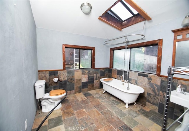 bathroom featuring toilet, tile walls, a skylight, and a bath