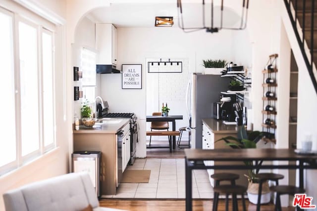 kitchen featuring white cabinetry, light tile patterned floors, stainless steel dishwasher, and sink