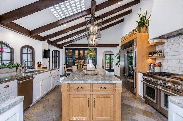 kitchen with beam ceiling, sink, a kitchen island, white cabinets, and high end appliances