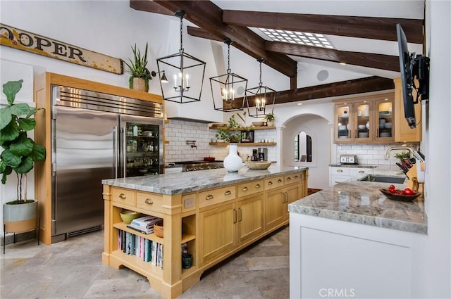 kitchen with pendant lighting, light stone counters, built in refrigerator, and sink