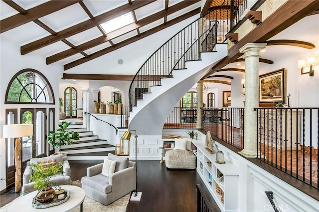 interior space featuring wood-type flooring, a towering ceiling, ornate columns, and beam ceiling