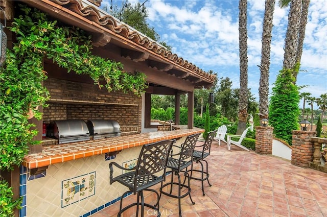 view of patio with area for grilling, a bar, and exterior kitchen