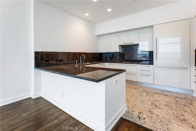 kitchen with kitchen peninsula, tasteful backsplash, stainless steel gas cooktop, dark wood-type flooring, and white cabinetry