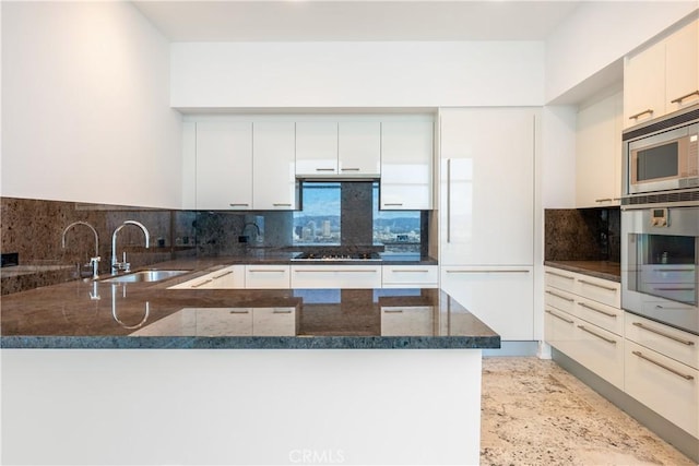 kitchen with kitchen peninsula, stainless steel appliances, dark stone counters, and sink