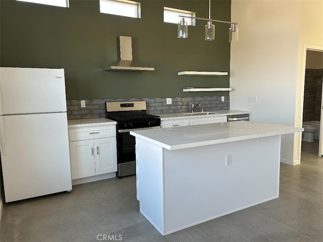 kitchen with stainless steel gas stove, wall chimney range hood, white refrigerator, white cabinets, and sink