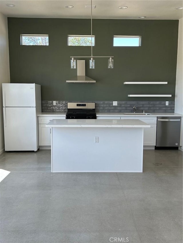 kitchen featuring white cabinets, decorative light fixtures, wall chimney range hood, stainless steel appliances, and sink