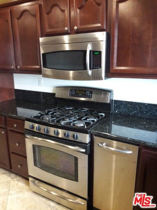 kitchen featuring light tile patterned flooring, stainless steel appliances, and dark stone counters