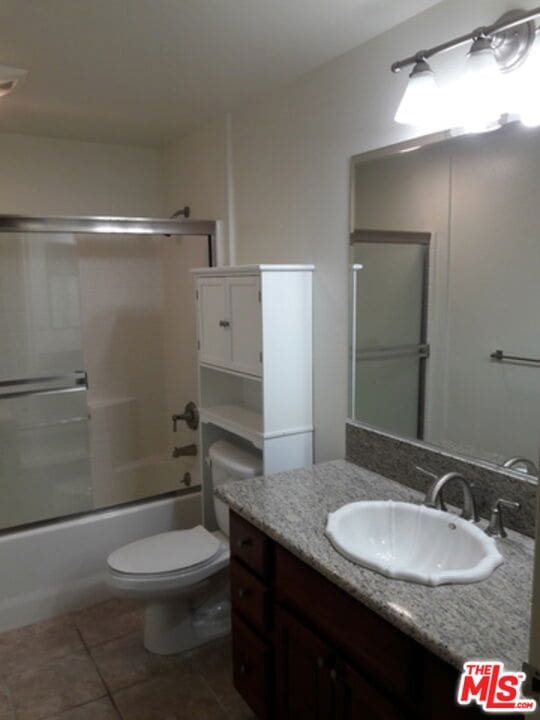 full bathroom featuring tile patterned flooring, vanity, toilet, and bath / shower combo with glass door