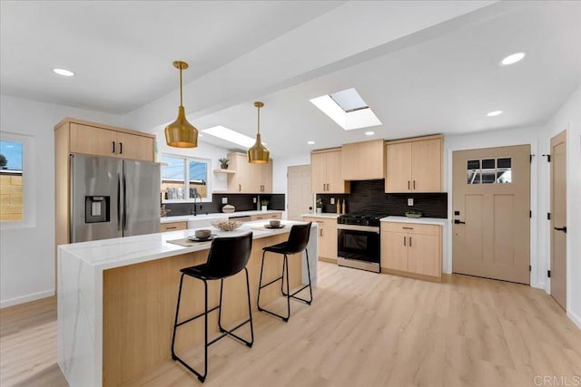 kitchen with light hardwood / wood-style floors, appliances with stainless steel finishes, pendant lighting, a skylight, and light brown cabinetry