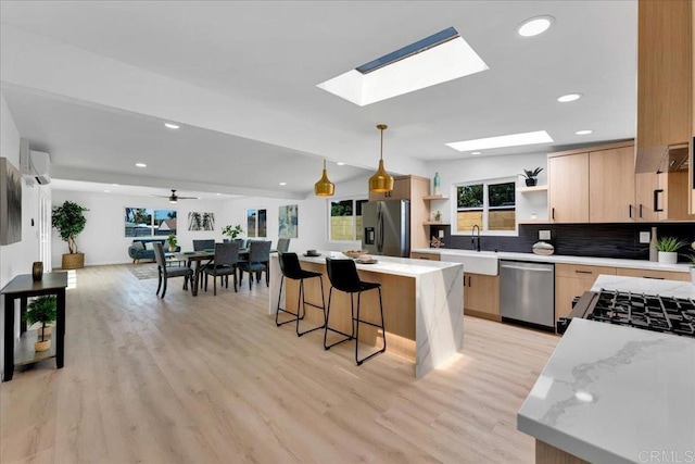 kitchen featuring ceiling fan, stainless steel appliances, hanging light fixtures, a center island, and a skylight