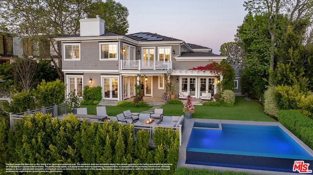 back house at dusk featuring an outdoor living space, solar panels, french doors, a balcony, and a patio