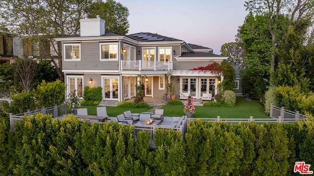 back house at dusk with outdoor lounge area, solar panels, french doors, a balcony, and a patio area