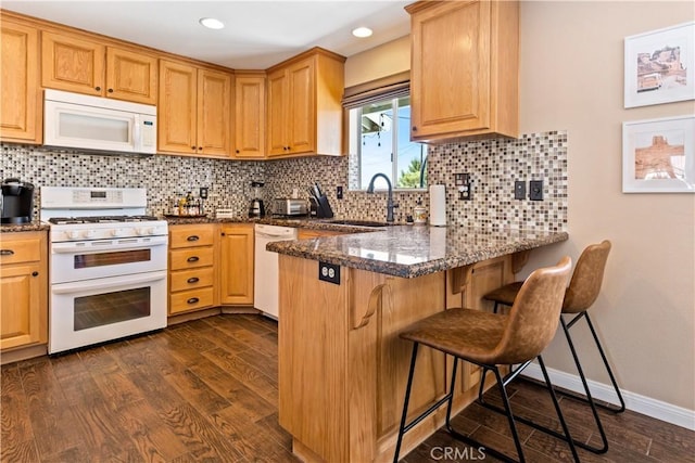 kitchen with white appliances, dark hardwood / wood-style flooring, dark stone counters, sink, and a kitchen breakfast bar