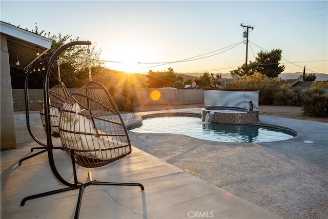 patio terrace at dusk featuring a swimming pool with hot tub