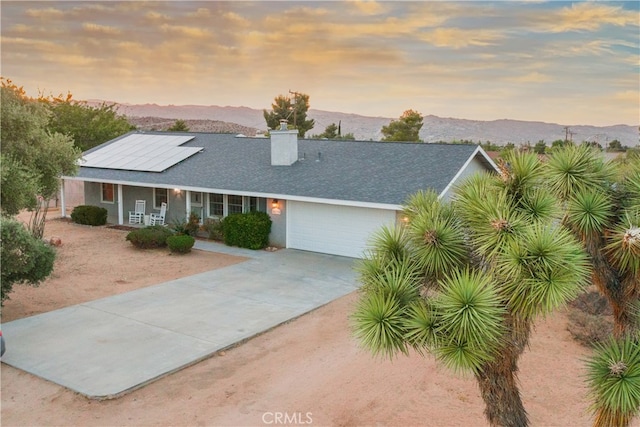 view of front of home with covered porch, a garage, a mountain view, and solar panels