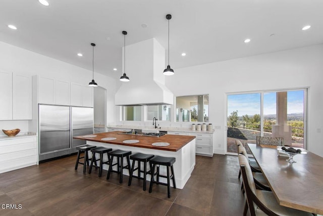 kitchen with wood counters, appliances with stainless steel finishes, dark wood-type flooring, white cabinets, and hanging light fixtures