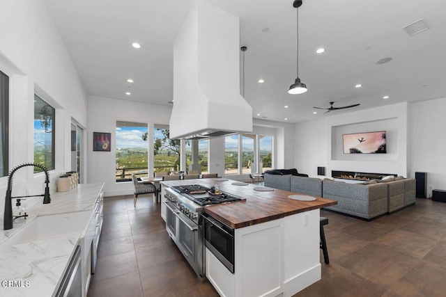 kitchen with wooden counters, custom range hood, stainless steel appliances, ceiling fan, and hanging light fixtures