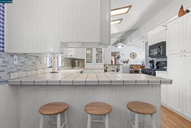 kitchen with a breakfast bar, tile countertops, kitchen peninsula, and black appliances