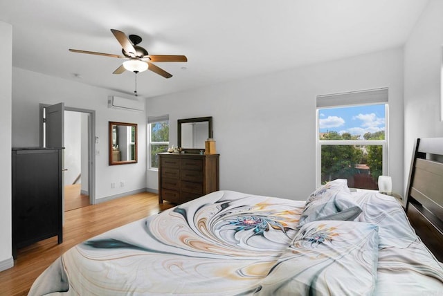 bedroom featuring multiple windows, light hardwood / wood-style floors, ceiling fan, and a wall unit AC