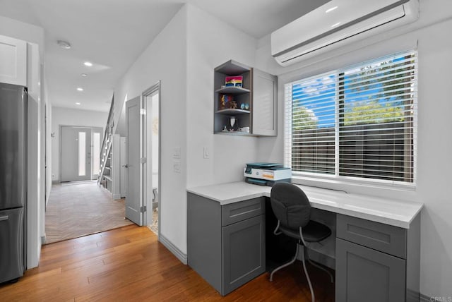 home office with light wood-type flooring, built in desk, and an AC wall unit