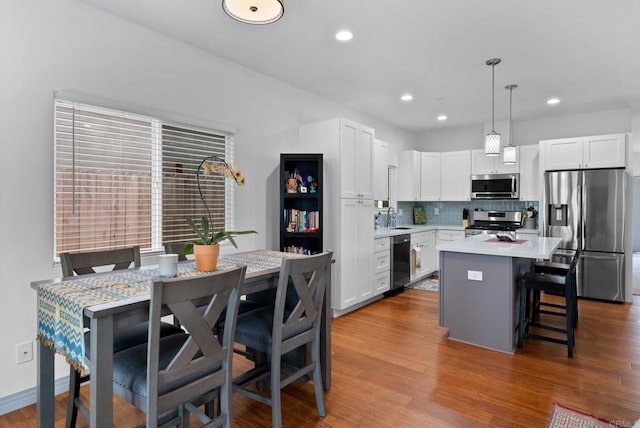 kitchen with pendant lighting, wood-type flooring, sink, white cabinetry, and stainless steel appliances