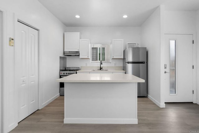 kitchen with range, sink, white cabinets, a kitchen island, and stainless steel refrigerator