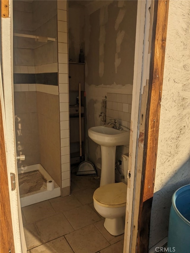 bathroom featuring tiled shower, backsplash, tile floors, sink, and toilet