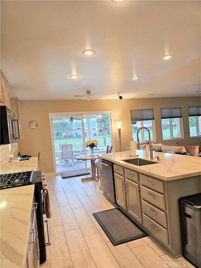 kitchen featuring light stone countertops, sink, gray cabinets, a center island with sink, and appliances with stainless steel finishes