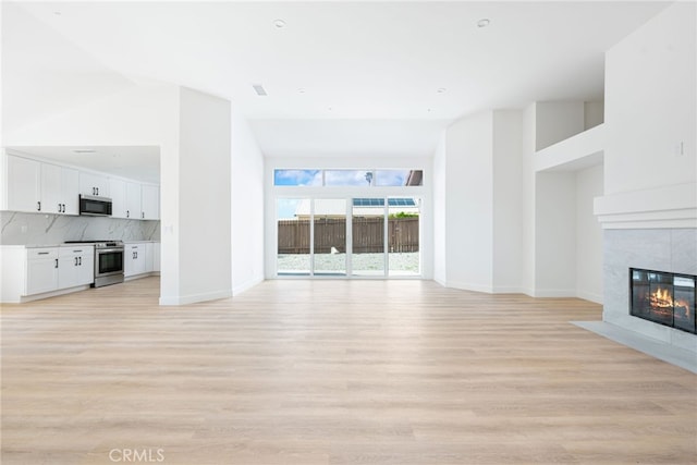 unfurnished living room featuring light hardwood / wood-style floors, high vaulted ceiling, and a tiled fireplace