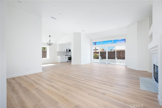 unfurnished living room featuring high vaulted ceiling, light hardwood / wood-style flooring, and a healthy amount of sunlight