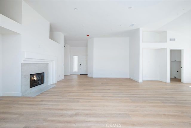 unfurnished living room featuring light hardwood / wood-style floors, a premium fireplace, and a towering ceiling