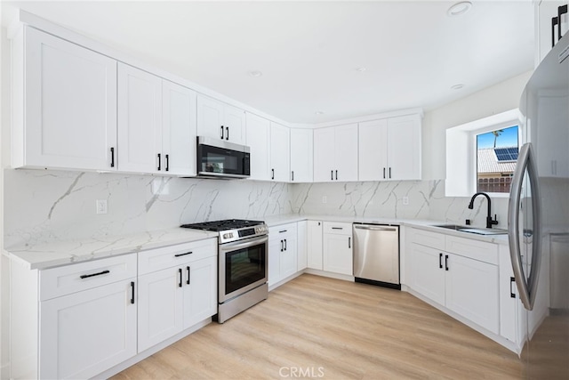 kitchen with white cabinetry, light stone countertops, sink, light hardwood / wood-style flooring, and appliances with stainless steel finishes