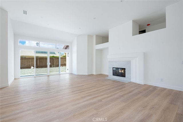 unfurnished living room featuring a tile fireplace, a high ceiling, and light wood-type flooring