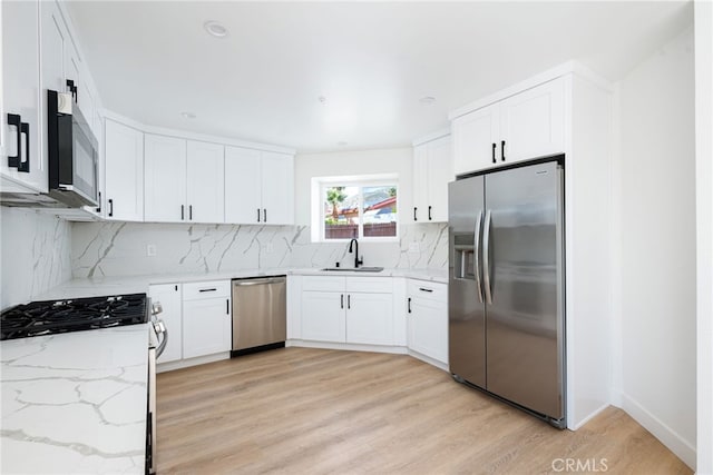 kitchen with white cabinetry, light stone countertops, sink, stainless steel appliances, and light hardwood / wood-style floors