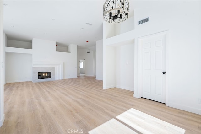 unfurnished living room with a towering ceiling, light hardwood / wood-style floors, and an inviting chandelier