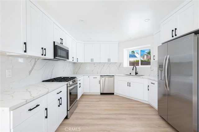 kitchen featuring sink, tasteful backsplash, light stone counters, light hardwood / wood-style floors, and appliances with stainless steel finishes